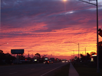 [This time the sky is full of clouds and the sun has reached the horizon so there is a swath of yellow on the right side of the image. The indentations and edges of the cloud blanket is highlighted so the color varies from yellow to orange to pink purple. The upper clouds are still dark purple with some pink undertones.]